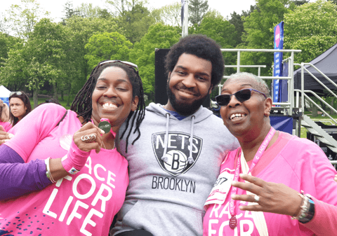 Dinny is celebrating finishing a Race for Life run with two others. She is smiling and holding a medal.