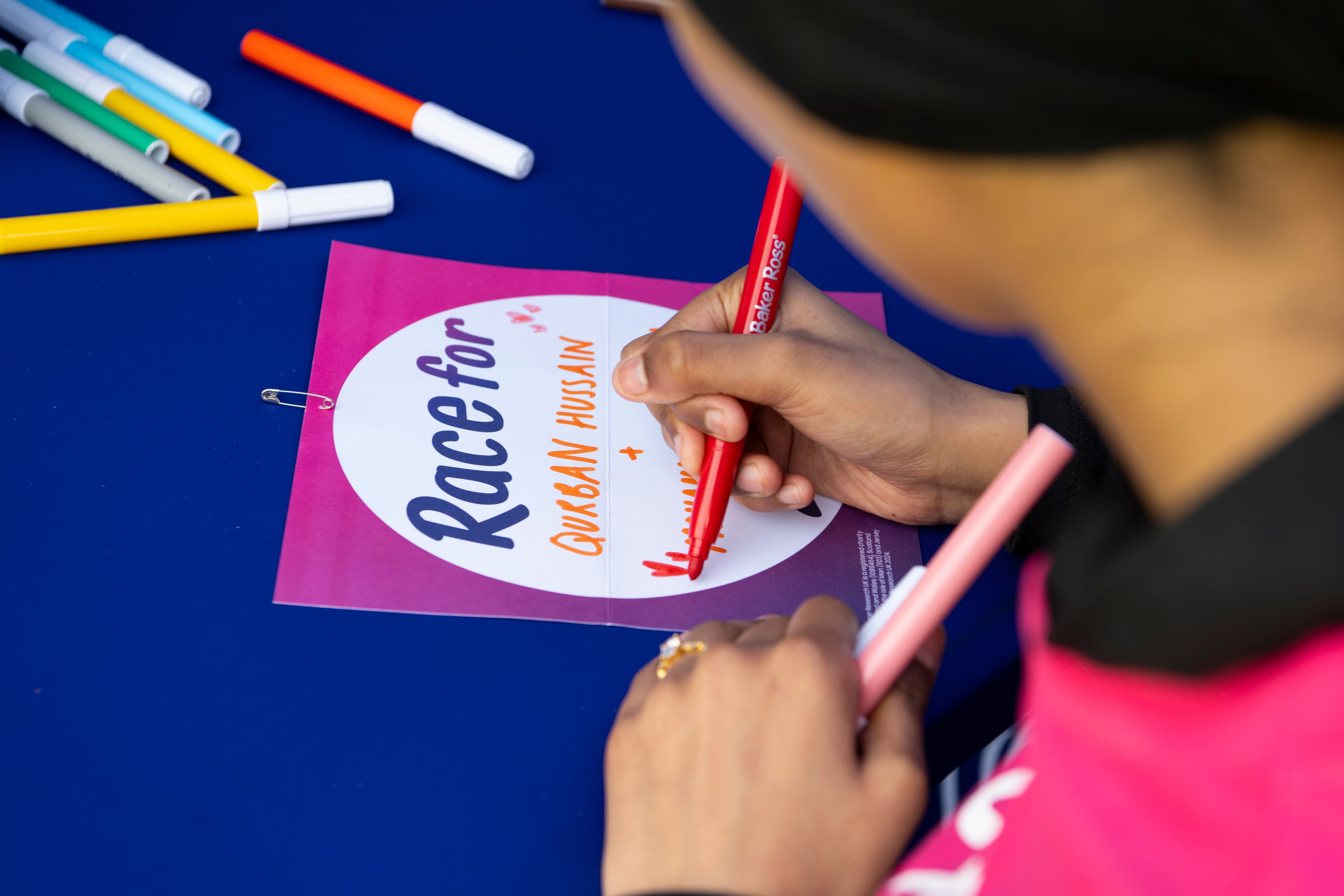 A lady writing the name of her loved one on her Race for Life back sign.
